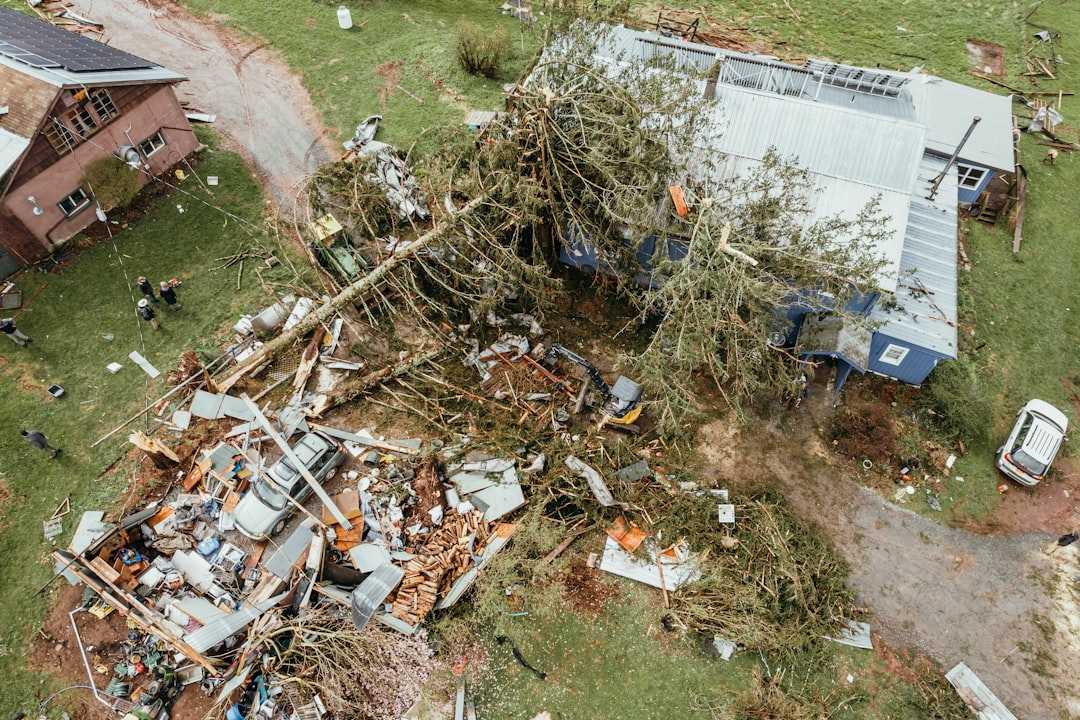 storm damaged house with missing roof shingles and debris